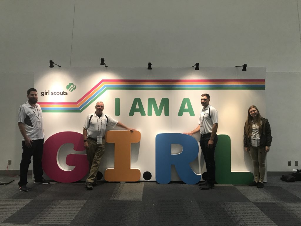 Four Evans employees stand in front of "I am a GIRL" sign.