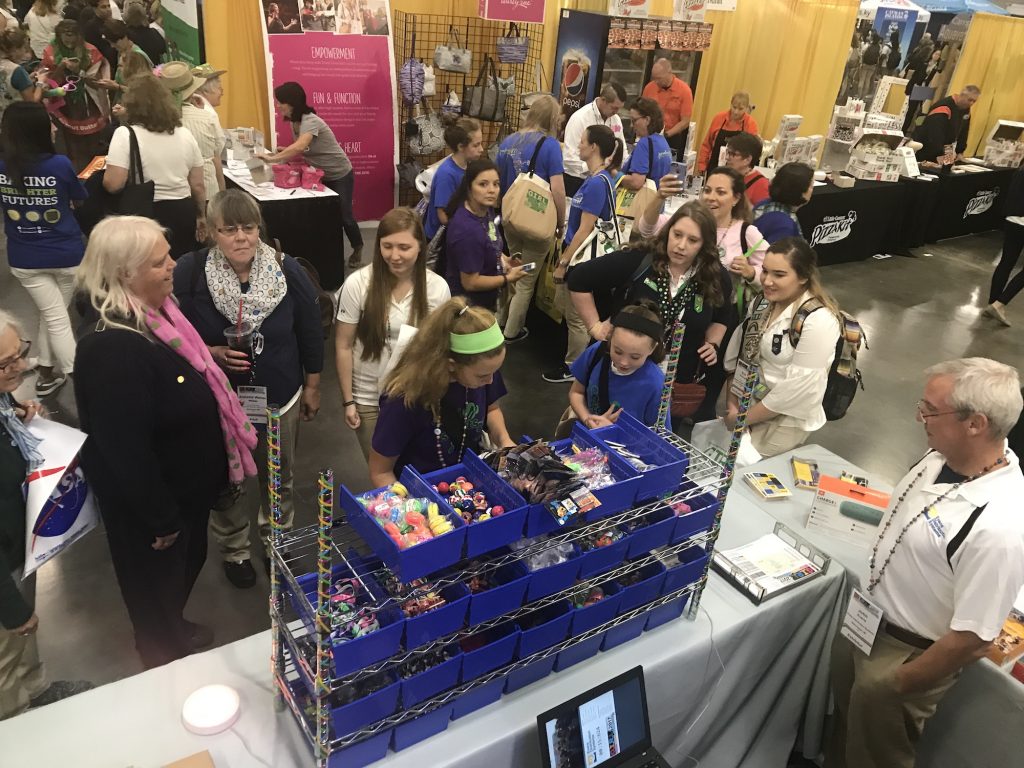 Group of girl scouts stands around pick and pack station at the GIRL convention.