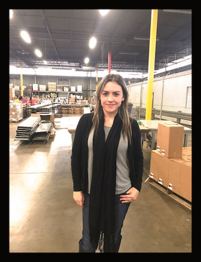 A girl stands in front of a background with warehouse activity