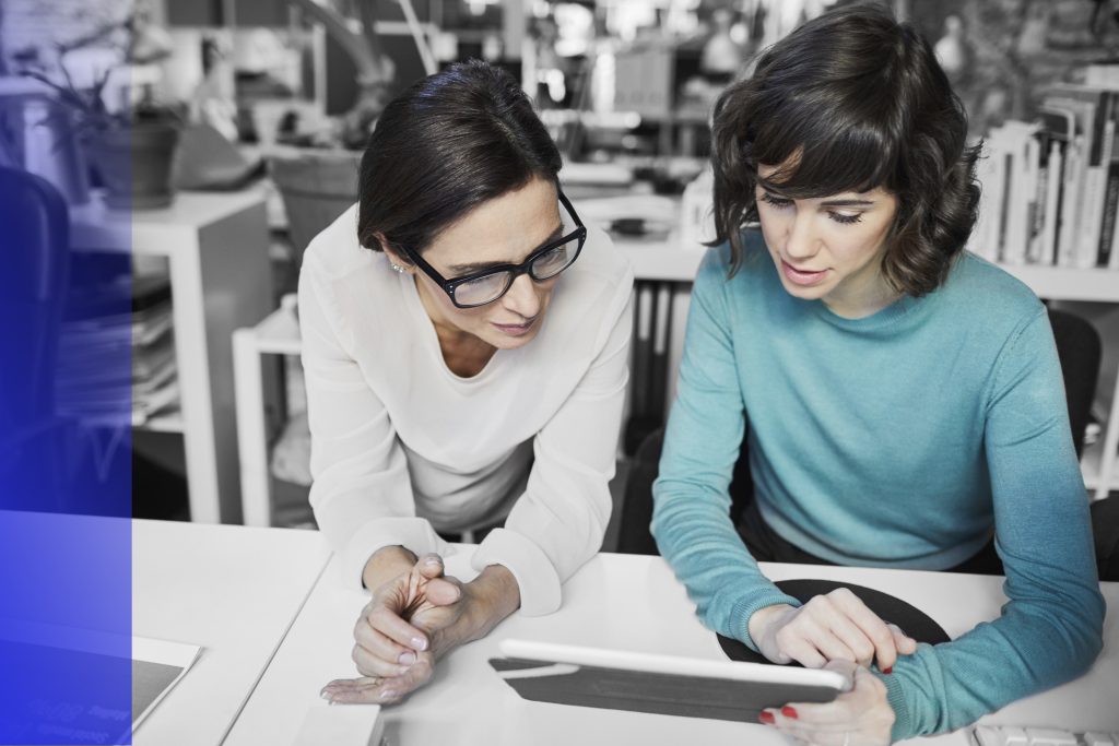 Two women sit next to each other looking at a tablet.