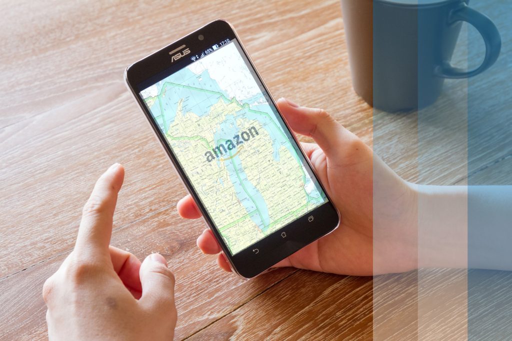 Hand holding phone. On the screen is the amazon logo, superimposed over a map of Michigan.